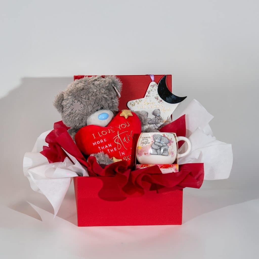 Valentine luxury gift box with teddy bear, love message heart, romantic mug, chocolates and decorative items in red and white packaging on a neutral background