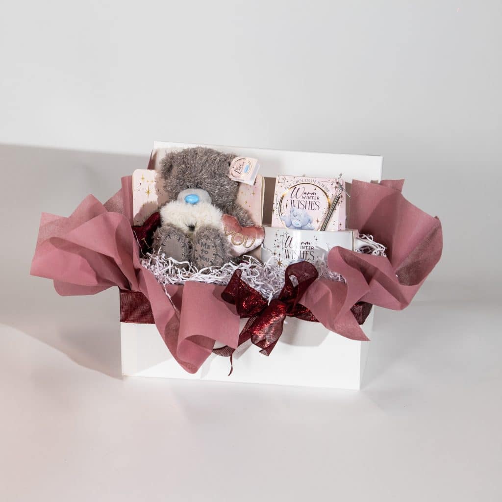 Valentine gift box with teddy bear, hot chocolate treats and romantic items in blush pink and burgundy luxury packaging on neutral background