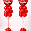 Pair of Valentine’s Day balloon columns with red heart-shaped foil balloons printed with “Happy Valentine’s Day” and red latex balloon clusters on a neutral background.