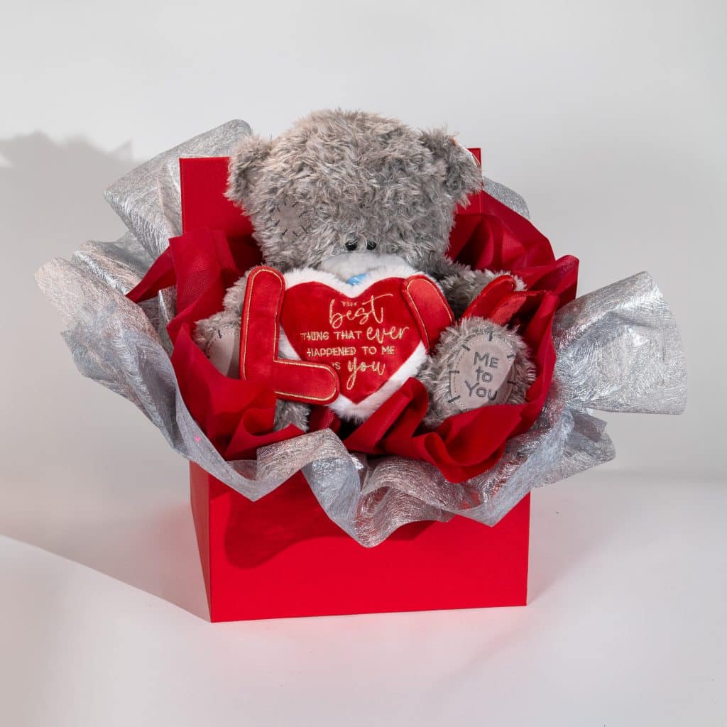 Valentine deluxe gift box with teddy bear holding love message heart and LOVE decoration in red and silver luxury packaging on neutral background