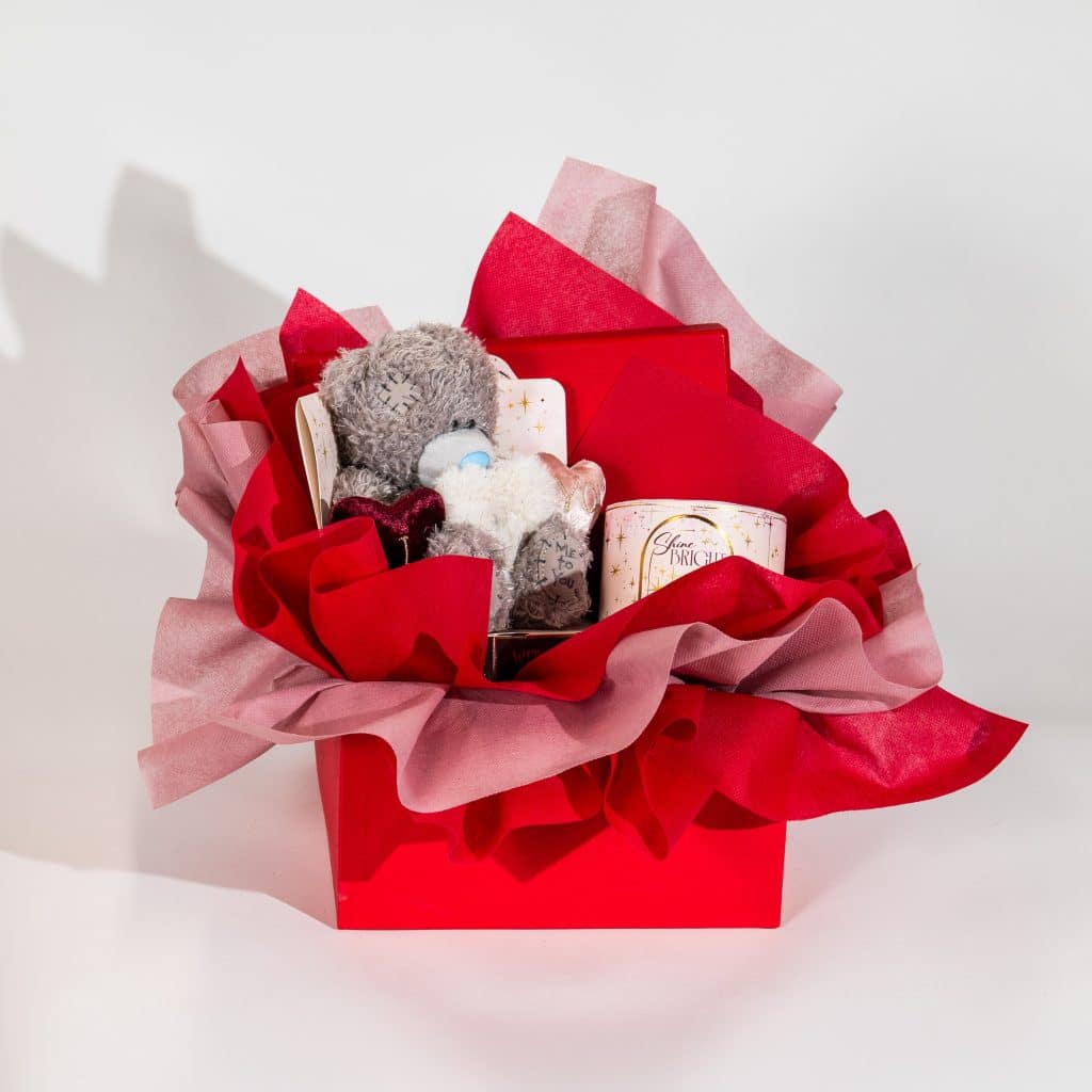 Valentine gift box with teddy bear, scented candle and romantic keepsakes in red and blush luxury packaging on neutral background