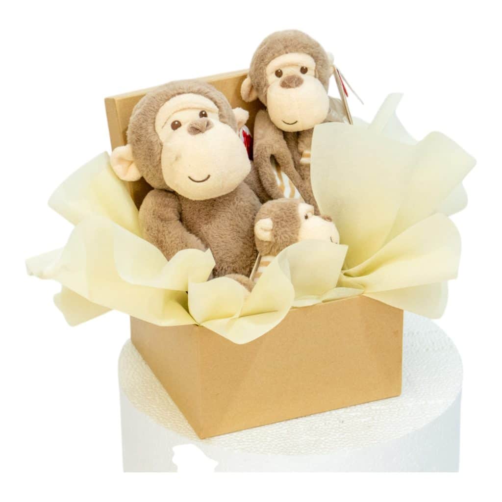 Baby gift box with three plush monkeys and soft yellow tissue paper.