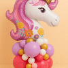 Unicorn-themed balloon arrangement with a large glittery foil unicorn balloon on top of a colorful base of lavender, fuchsia, gold, white, and peach latex balloons, perfect for fantasy-inspired celebrations.