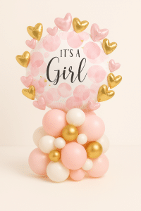 “It’s a Girl” pink and white balloon arrangement with heart foil accents in gold and pink, placed on a pastel base of blush, ivory, and gold balloons — perfect for baby girl celebrations.