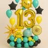 Balloon display with large gold “13” foil balloons, smiling sun foil, starburst accent, and “Happy Birthday” message, all set on a base of yellow, turquoise, and black balloons with space-themed elements.
