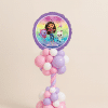 Gabby’s Dollhouse balloon tower with rainbow foil balloon featuring Gabby, Pandy Paws, and Cakey Cat, on a pink, lilac, and white spiral balloon base.