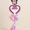 Minnie Mouse Happy Birthday heart foil balloon mounted on a pastel pink, lavender, and white twisted spiral balloon column with organic balloon clusters on a neutral background