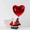 Valentine gift box with teddy bear holding I Love You heart, preserved forever rose in display box, black and red wrapping and large red heart foil balloon on neutral background