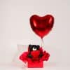 Red gift box with black teddy bear holding a heart and a large red helium heart balloon on a neutral studio background.