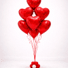 Floor-standing bouquet of red helium foil heart balloons tied with red ribbons on a decorative red and white balloon base, elegant Valentine’s balloon arrangement on a soft neutral background.