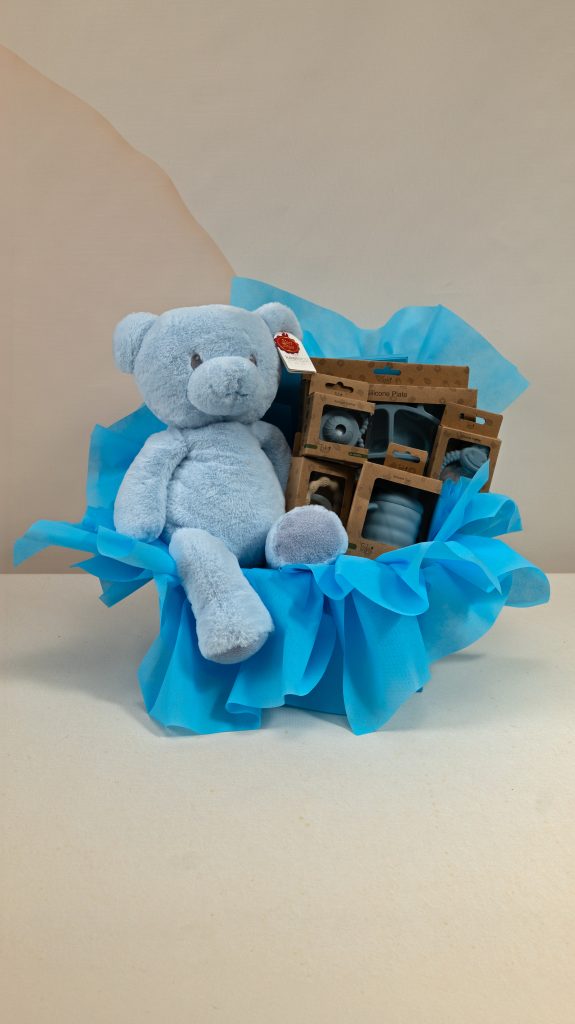 Deluxe baby boy gift box with blue Keel Toys teddy bear and AMEK Toys silicone plate, cup, cutlery and assorted teethers in blue gift wrapping.